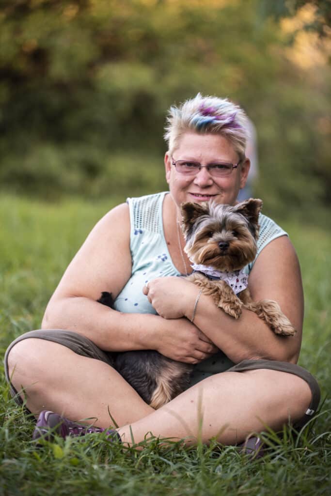 Gaál Vera virtuális asszisztens a fűben ülve Tofi nevű kutyájával.
